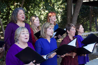 women in blue and purple tops singing music in front of greenery backdrop
